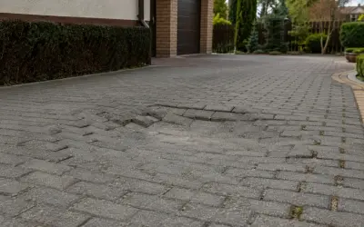 Zapadnięta kostka brukowa na podjeździe, z widocznym zagłębieniem i nierównościami.