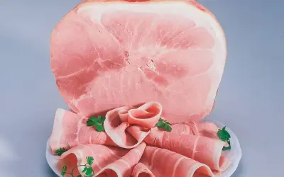 Fetta di prosciutto cotto, con fette arrotolate guarnite di prezzemolo. Attenzione: il prosciutto cotto è considerato cancerogeno.