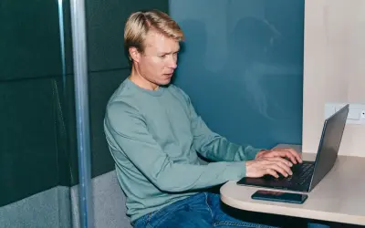 Man i ljudisolerad bås jobbar intensivt på laptop, kanske funderar på konsekvenserna av illojalitet mot arbetsgivare och skadestånd.