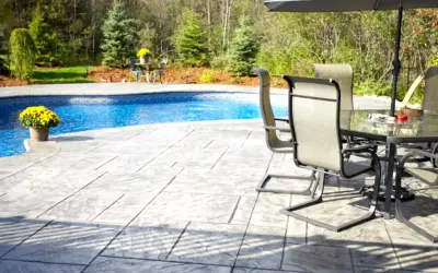 Un'area piscina con **cemento stampato carrabile** che imita la pietra, tavoli e sedie sotto un ombrellone.