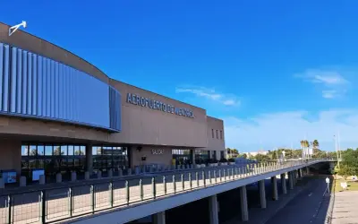 Nowoczesny budynek lotniska Aeropuerto de Menorca z napisem "AEROPUERTO DE MENORCA" i podjazdem pod niebo.