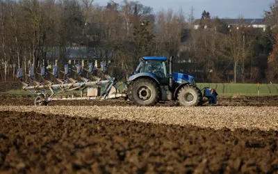 Niebieski traktor z pługiem orze pole. Rolnik przygotowuje ziemię, zastanawiając się, do kiedy można orać pole arimr.