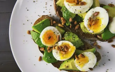 Avokado recept: två rostade brödskivor med avokado, kokt ägg och pinjenötter, strösslade med peppar.