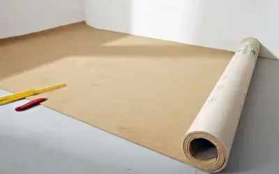 Werkzeug liegt bereit für das Teppich verlegen. Ein Teppichboden wird ausgerollt, daneben ein Zollstock und ein Cuttermesser.