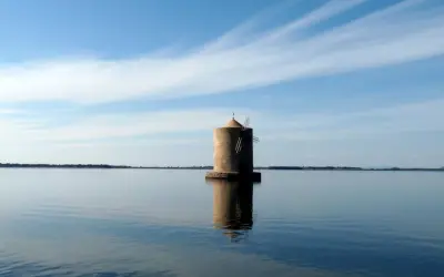 Mulino solitario nella laguna di Orbetello, con cielo azzurro e nuvole sottili.