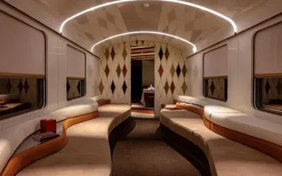 Luxuriöses Interieur eines Nachtzugs nach Italien mit geschwungenen Sofas, Rautenmuster-Tapete und indirekter Beleuchtung.