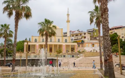 Plac z fontannami i palmami przed meczetem w Durrës, Albania. Ludzie spacerują po schodach.