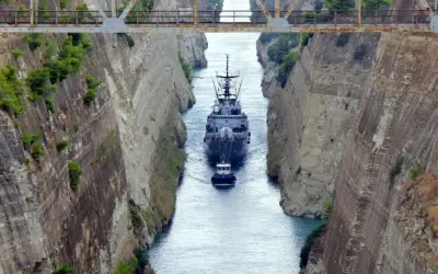 Una nave militare e un rimorchiatore navigano nel **Canale di Corinto**, tra alte pareti rocciose scavate dall'uomo.