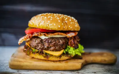 Soczysty burger wołowy z bekonem, serem, pomidorem i sałatą na desce.