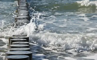 Fale rozbijają się o drewniane pale na plaży. Piękna, czerwcowa pogoda zachęca do spacerów brzegiem morza.