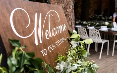 Drewniana tablica "Welcome to our wedding" z zielonymi liśćmi. Zastanawiasz się, kogo zaprosić na wesele?