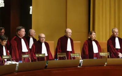Siedmiu sędziów w togach, w tym jedna kobieta, stoi w sali sądowej. Wszyscy mają na sobie białe żaboty. W tle widać złote zasłony.