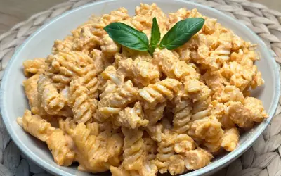 Fusilli conditi con una cremosa salsa al pesto e pomodorini, guarniti con foglie di basilico fresco.
