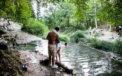 Persone si rilassano nelle acque termali dei Bagni di San Filippo, immersi nel verde di un bosco.