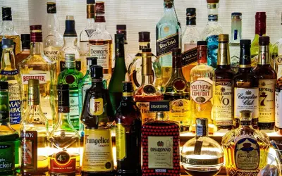 Różnorodne rodzaje alkoholi: whisky, likiery, gin, brandy i inne, stojące na półce.