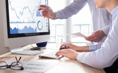 Dwóch analityków analizuje wykresy giełdowe na monitorze, dyskutując o strategii buy limit co to.