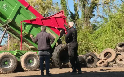 Deux hommes supervisent le déchargement d'une remorque verte remplie de pneus usagés, une étape clé du recyclage des pneus.