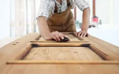 Carpintero lijando una puerta de sapelly para modernizarla, revelando la veta de la madera.