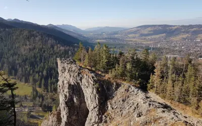 Widok z Nosala, góry samobójców, na Tatry i Zakopane. Skalisty szczyt, las i dolina.