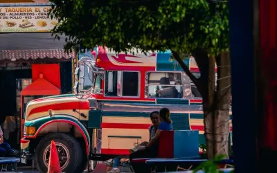 Bunter "chicken bus" in Guatemala, bereit für die nächste Fahrt. Menschen warten auf dem Bürgersteig.
