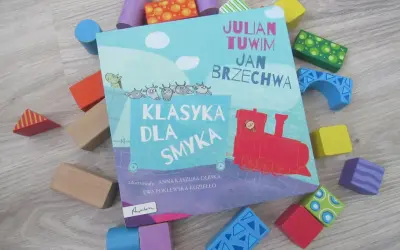 Książka "Klasyka dla smyka" z wierszami Tuwima i Brzechwy, otoczona kolorowymi klockami. Czytanie jej to jak zabawa, a nie jak szukanie karaluchów pod poduchy.