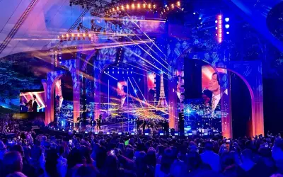 Koncertowa scena z tłumem widzów, oświetlona niebieskimi i różowymi światłami, z ekranami wyświetlającymi obrazy i wieżę Eiffla.