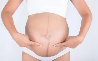 Kreska na brzuchu w ciąży, symbol przemiany. Dwie dłonie wskazują na ciemną linię biegnącą przez środek.