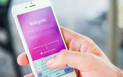 Dłoń trzyma smartfon z ekranem logowania Instagram. Widoczna opcja "Zapomniane dane logowania?" podpowiada, jak odzyskać hasło na Instagramie.