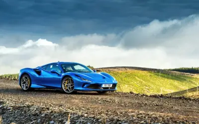 Niebieskie Ferrari F8 na tle malowniczego, pagórkowatego krajobrazu z chmurami na niebie.