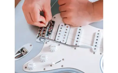 Ręce montują struny do mostka gitary elektrycznej. To ważny krok, jak zrobić gitarę elektryczną, by brzmiała idealnie.