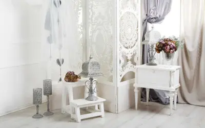 Delikatny salon w stylu shabby chic. Białe meble, ażurowa parawan, świeże kwiaty i ozdobne latarenki tworzą romantyczny nastrój.