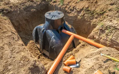 Instalacja szamba w wykopie. Pomarańczowe rury drenarskie i przyłącza czekają na montaż. Trwa praca nad tym, na jakiej głębokości drenaż odwadniający będzie skuteczny.