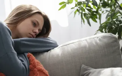 En ung kvinna med utmattningssyndrom symtom vilar på en soffa, ser trött och nedstämd ut.