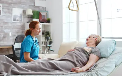 Pielęgniarka rozmawia z pacjentką leżącą w łóżku. W tle widać kule, co sugeruje, że pacjentka może potrzebować wsparcia w odżywianiu dojelitowym.