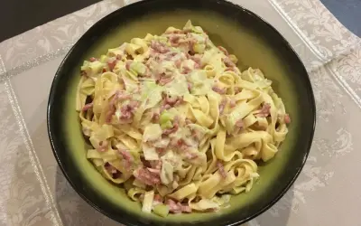 Un plat de tagliatelle poireaux crémeuses avec des lardons, servi dans un bol vert.