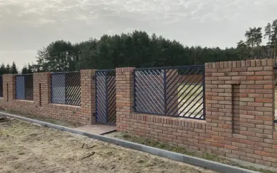 Solidne ogrodzenie z cegły z ozdobnymi metalowymi przęsłami, tworzące elegancką barierę przed lasem.