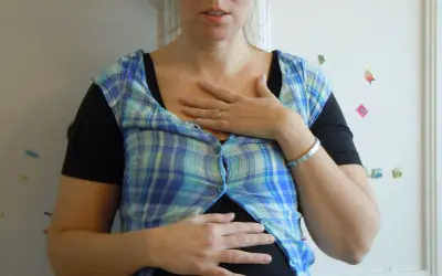En kvinna med en rutig skjorta över en svart topp, håller händerna över magen. Hon ser ut att vara **rennie gravid**.