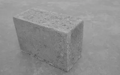 Szary bloczek betonowy na szarym tle. Jego wymiary są standardowe, idealny do budowy.