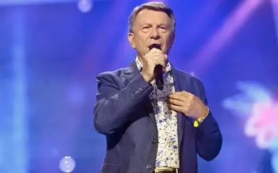Wojciech Gąsowski w niebieskiej marynarce i kwiecistej koszuli śpiewa do mikrofonu na tle niebieskiej sceny.