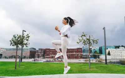 Kobieta w białym stroju sportowym wykonuje bieg w miejscu na tle miejskiego krajobrazu.