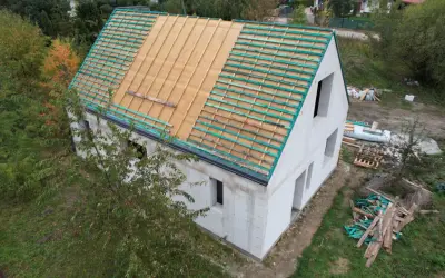 Dom w budowie, widoczne etapy budowy domu: ściany z bloczków, przygotowany dach pod pokrycie.