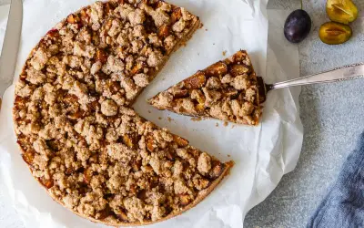 Ein köstlicher, gesunder Pflaumenkuchen mit knuspriger Streuseldecke. Ein Stück wird gerade herausgehoben.