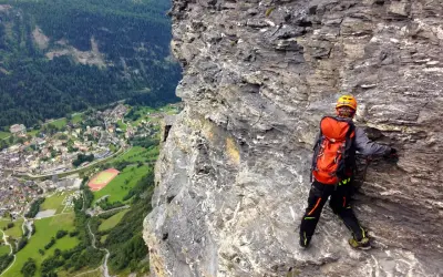 Wspinaczka via ferrata w Szwajcarii. Widok na dolinę i miasteczko z perspektywy skalnej ściany.