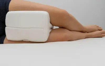 En person sover med ryggskott, med en vit kudde mellan knäna för stöd.