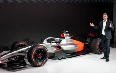 Ein Mann präsentiert stolz ein futuristisches Formel 1 Auto in Silber und Orange.