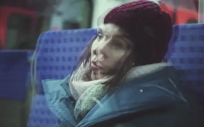 Kobieta w czapce i szaliku, siedząca w pociągu. Jej twarz jest rozmyta, jakby doświadczała amnezji dysocjacyjnej, zagubiona w myślach.