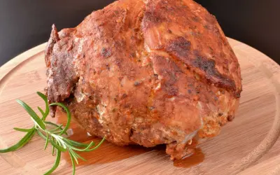 Pieczona szynka z ziołami, która wygląda jakby była przygotowana z użyciem marynaty do szynki. Gałązka rozmarynu dodaje aromatu.