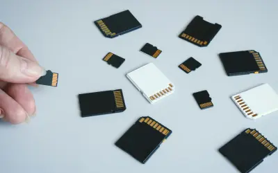 Różne karty pamięci, w tym micro SD, leżą na jasnym tle. Jedna karta jest trzymana w palcach. To jest karta pamięci.