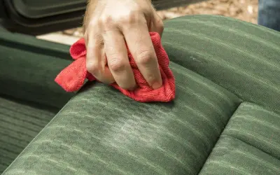 Dłoń z czerwoną ściereczką czyści zieloną tapicerkę. Domowy płyn do czyszczenia tapicerki działa cuda!