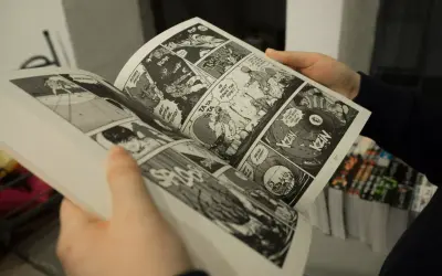 Des mains tiennent un manga ouvert, révélant des cases de bande dessinée pleines d'action. Apprendre comment lire un manga est facile avec ces images dynamiques.